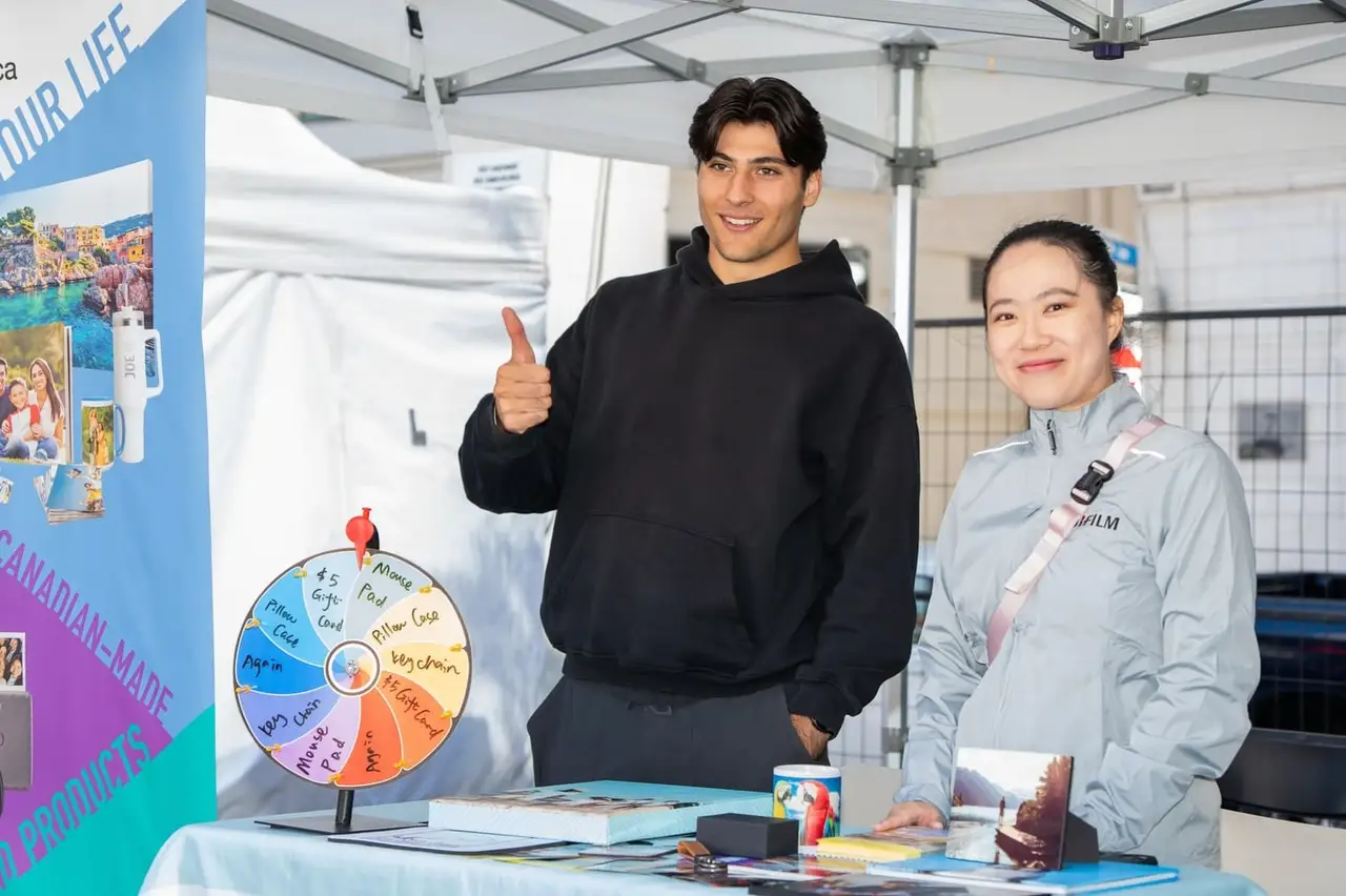 Two people give a thumbs-up at an information stand with a prize wheel.