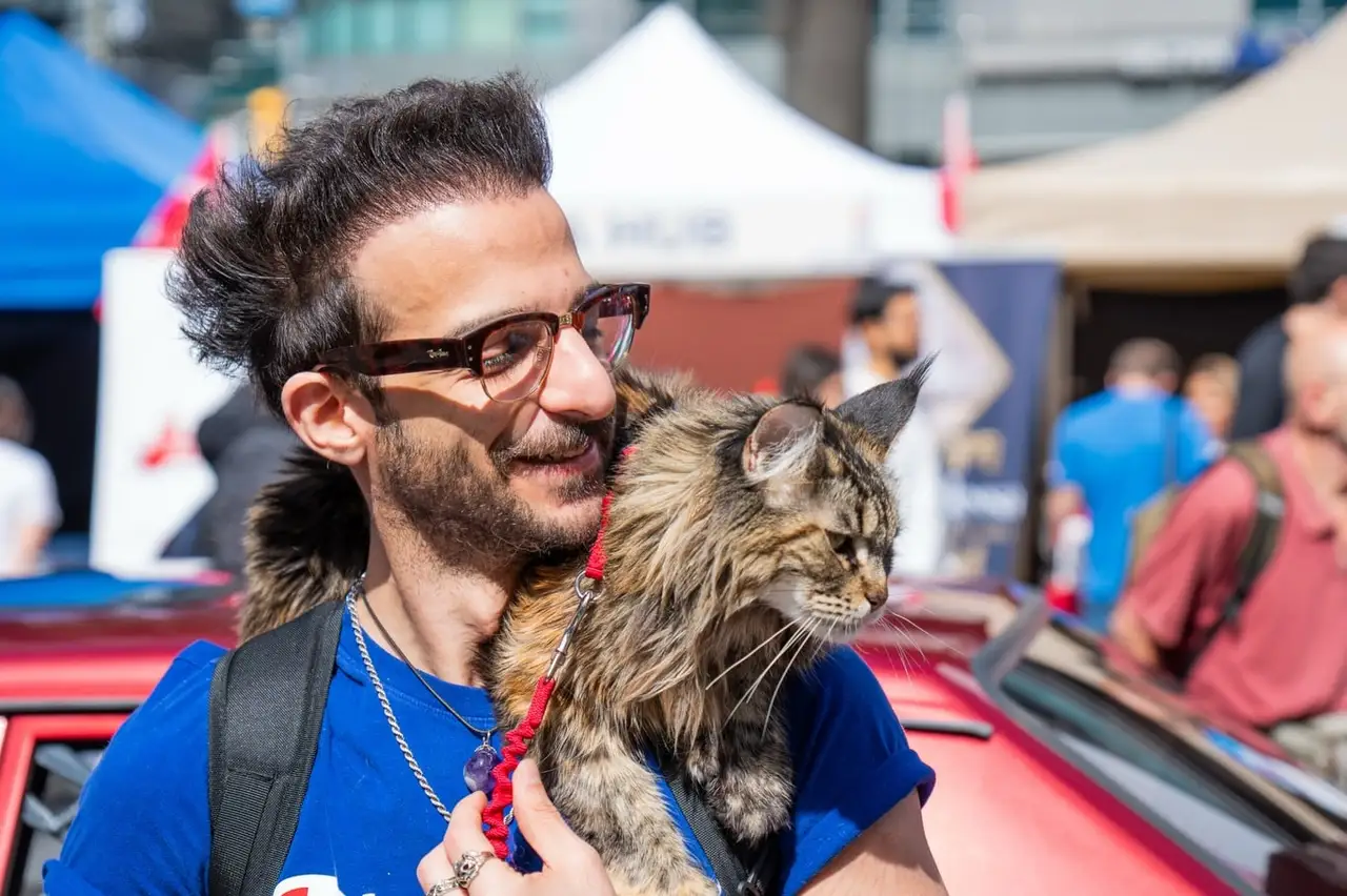 A visitor in glasses carries a long-haired cat on his shoulder through the festival.