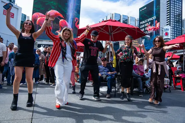 Visitors dance together in the open middle of the square, red umbrellas behind them.