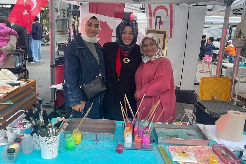 An ebru (marbling) table with trays of water, brushes and jars of paint, three women standing behind it.