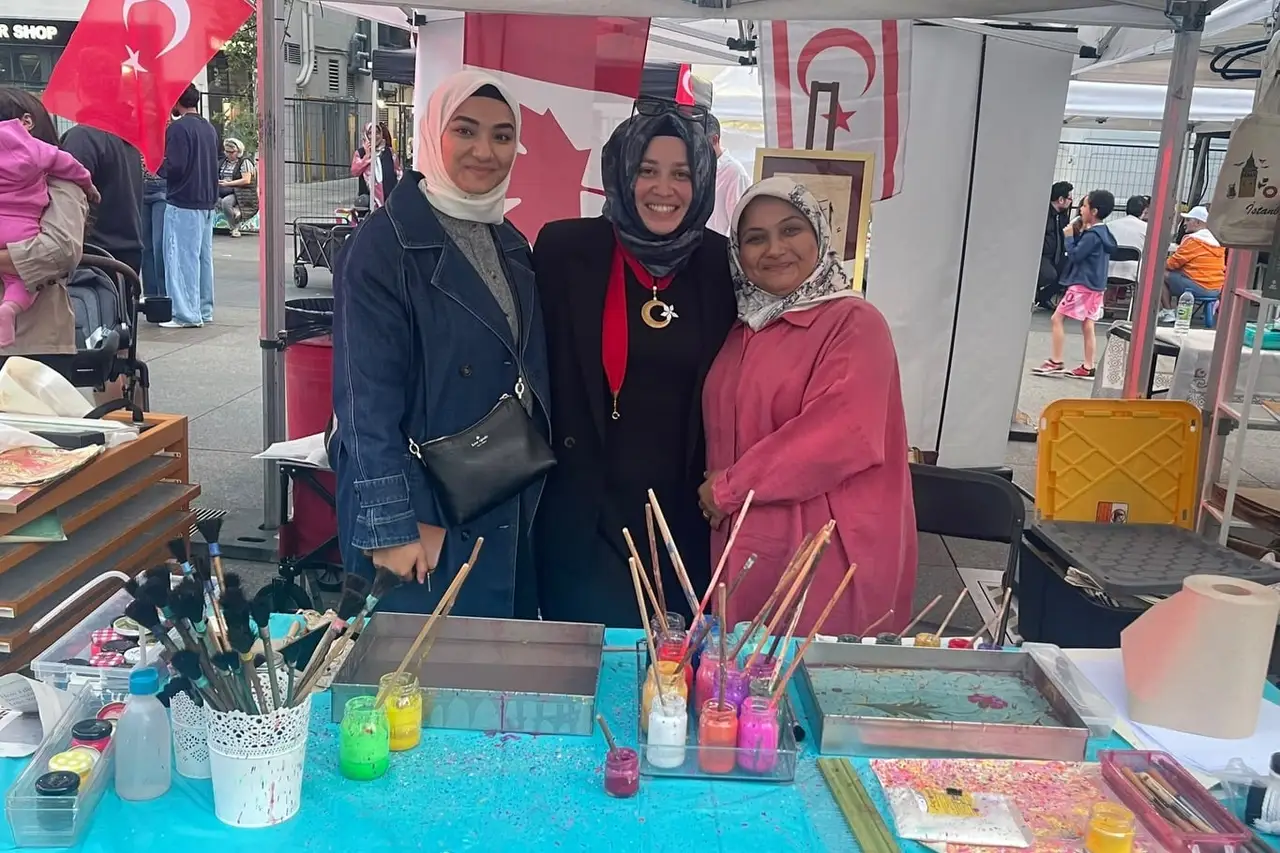 An ebru (marbling) table with trays of water, brushes and jars of paint, three women standing behind it.