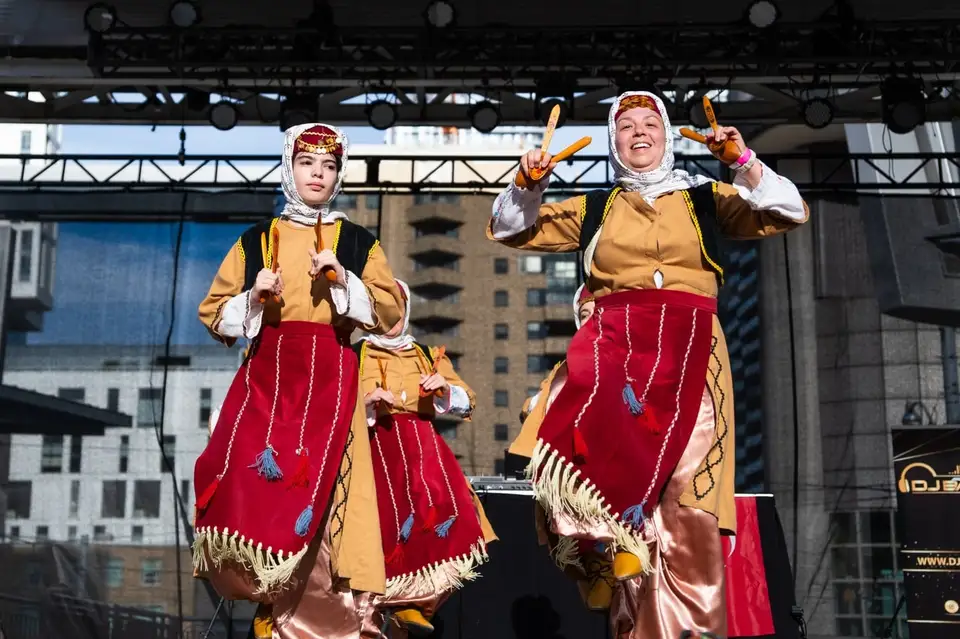 Two dancers in red-and-gold costumes and white headscarves wave from the stage.