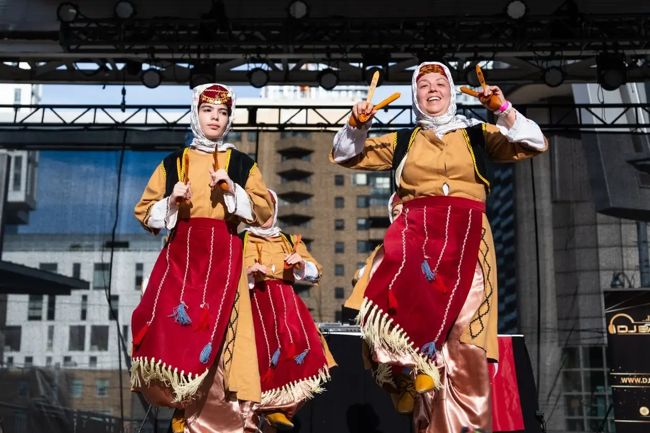 Two dancers in red-and-gold costumes and white headscarves wave from the stage.