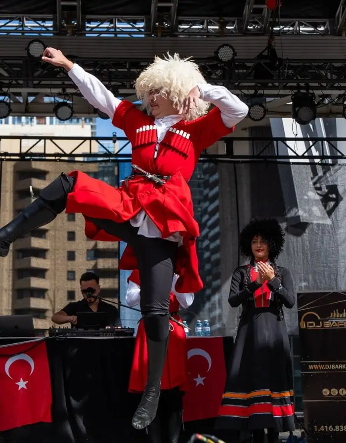 A dancer in a red costume and white fur hat mid-leap on the main stage, a Turkish flag hanging from the DJ table below.