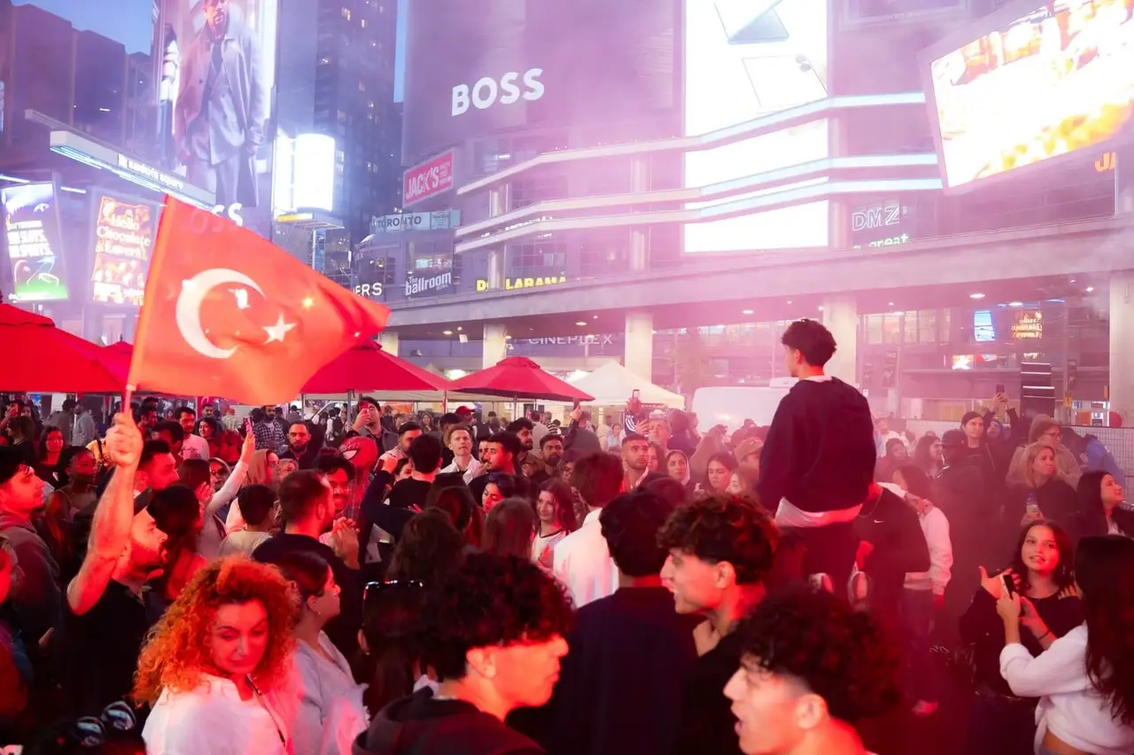 The evening crowd under red stage light, a Turkish flag held up above them.