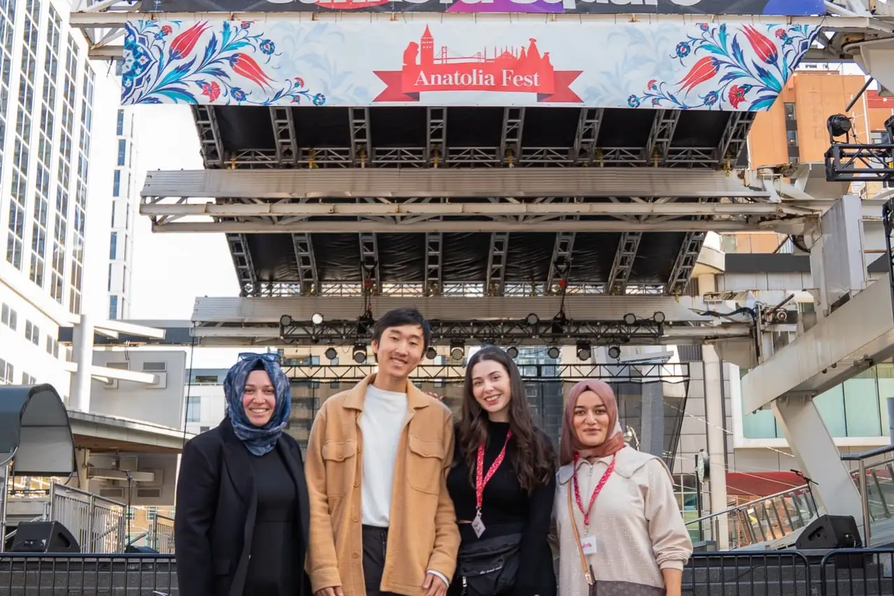 Four visitors in front of the main stage, the Anatolia Fest banner with tulip ornaments across its top.
