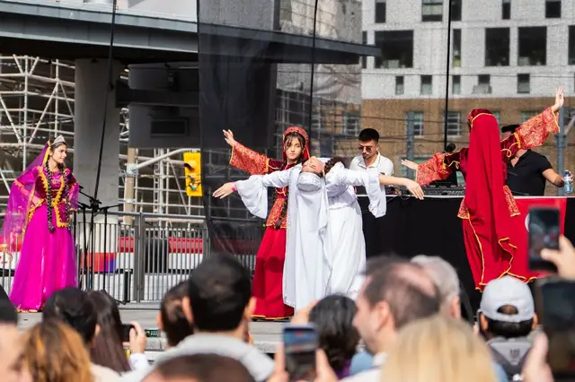 Dancers in white and red perform on stage while the audience in front films on their phones.