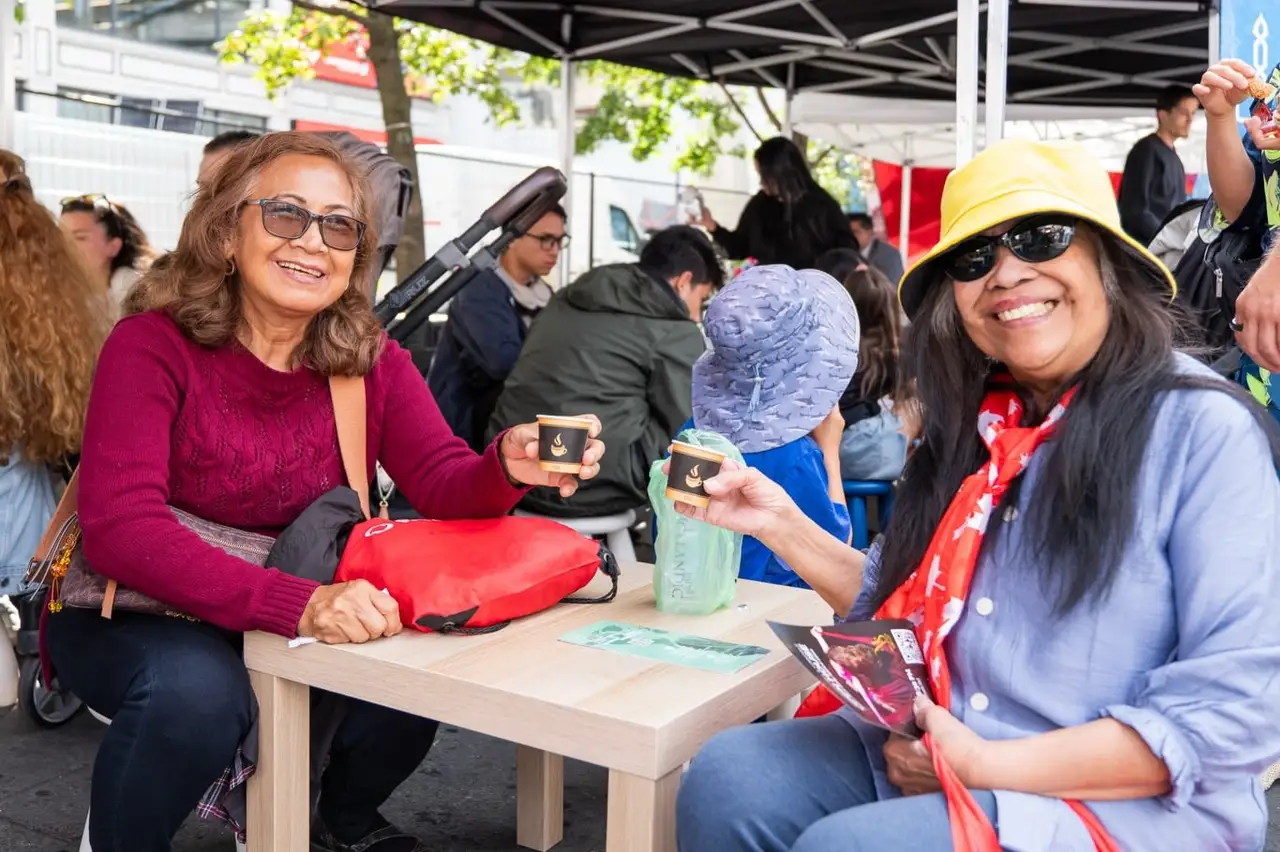 Two women laugh together at a small table in the festival’s seating area.