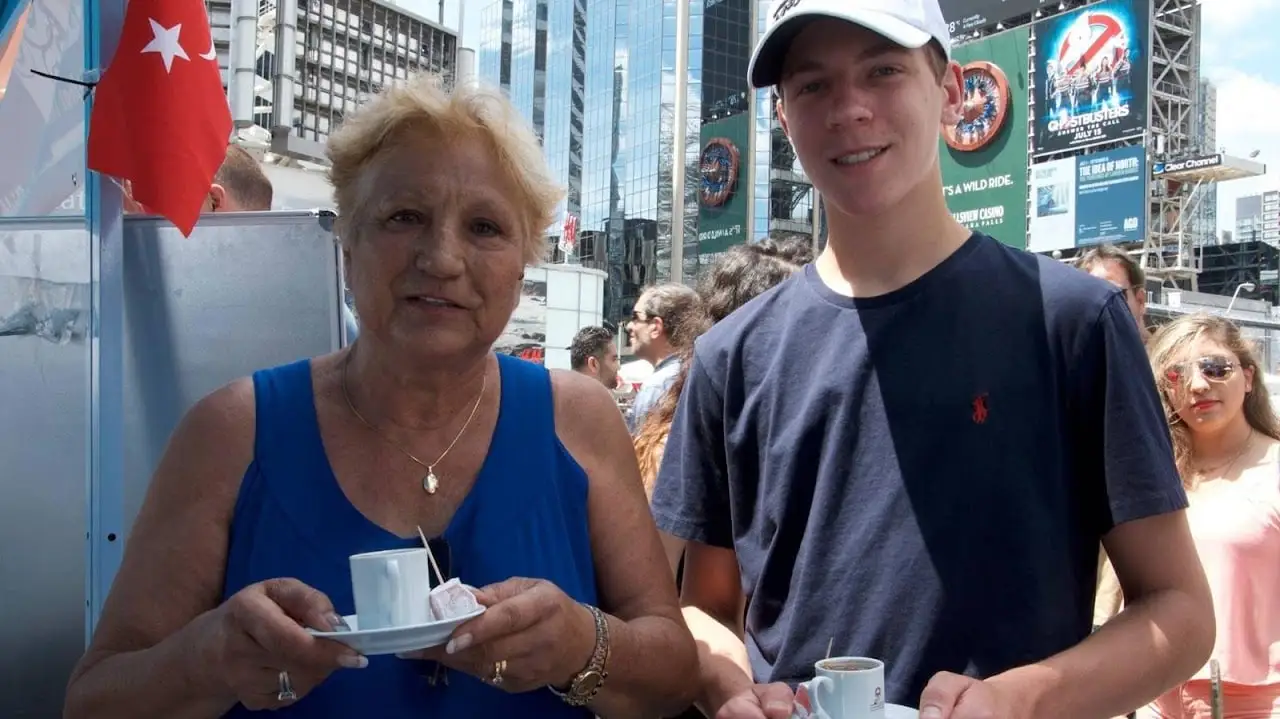 An older woman and a teenager hold small cups of Turkish coffee, a Turkish flag behind them.
