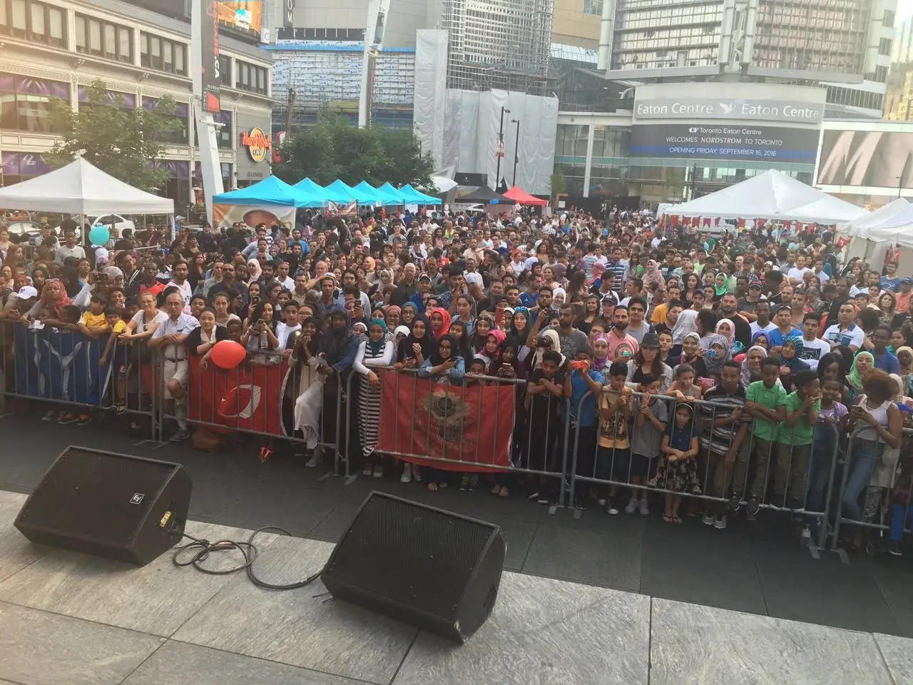 A packed crowd behind the stage barriers on Yonge-Dundas Square, Turkish flags hung along the fence.