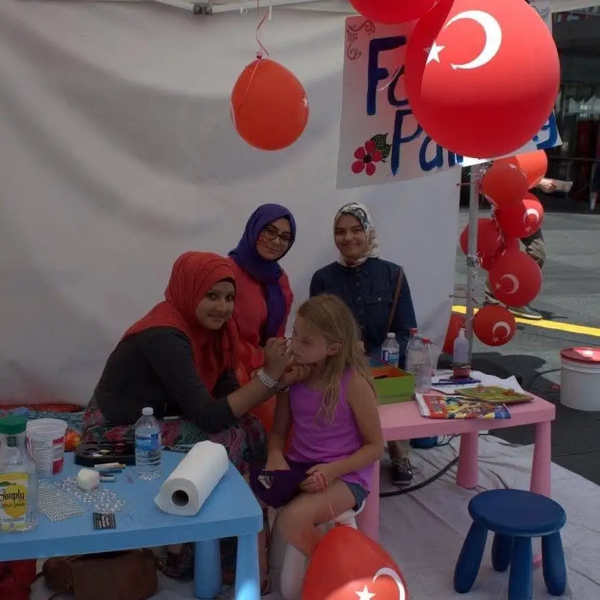 Face painting at the kids’ corner, red balloons with the crescent and star overhead.