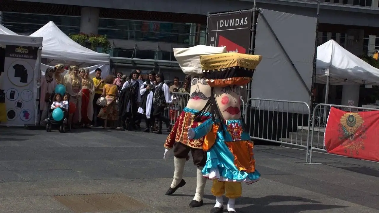 A costumed giant figure in bright robes walks across the square.
