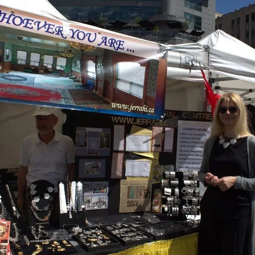 A jewellery stand under the market tents, a man and a woman standing beside it.