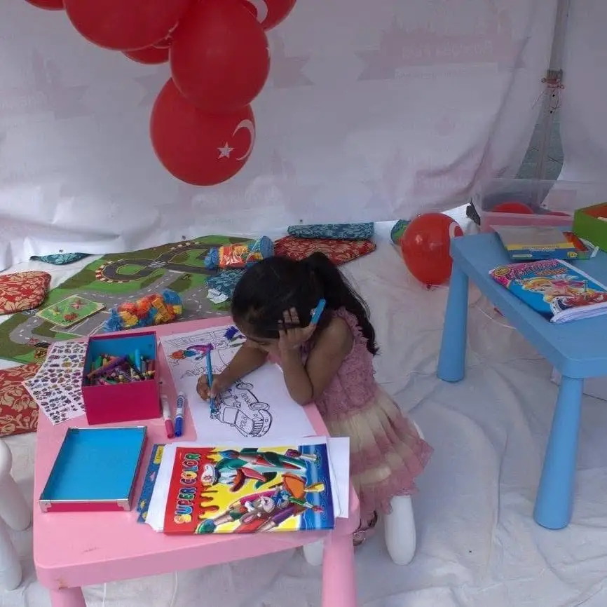A child bent over a colouring sheet at the kids’ table, red balloons overhead.