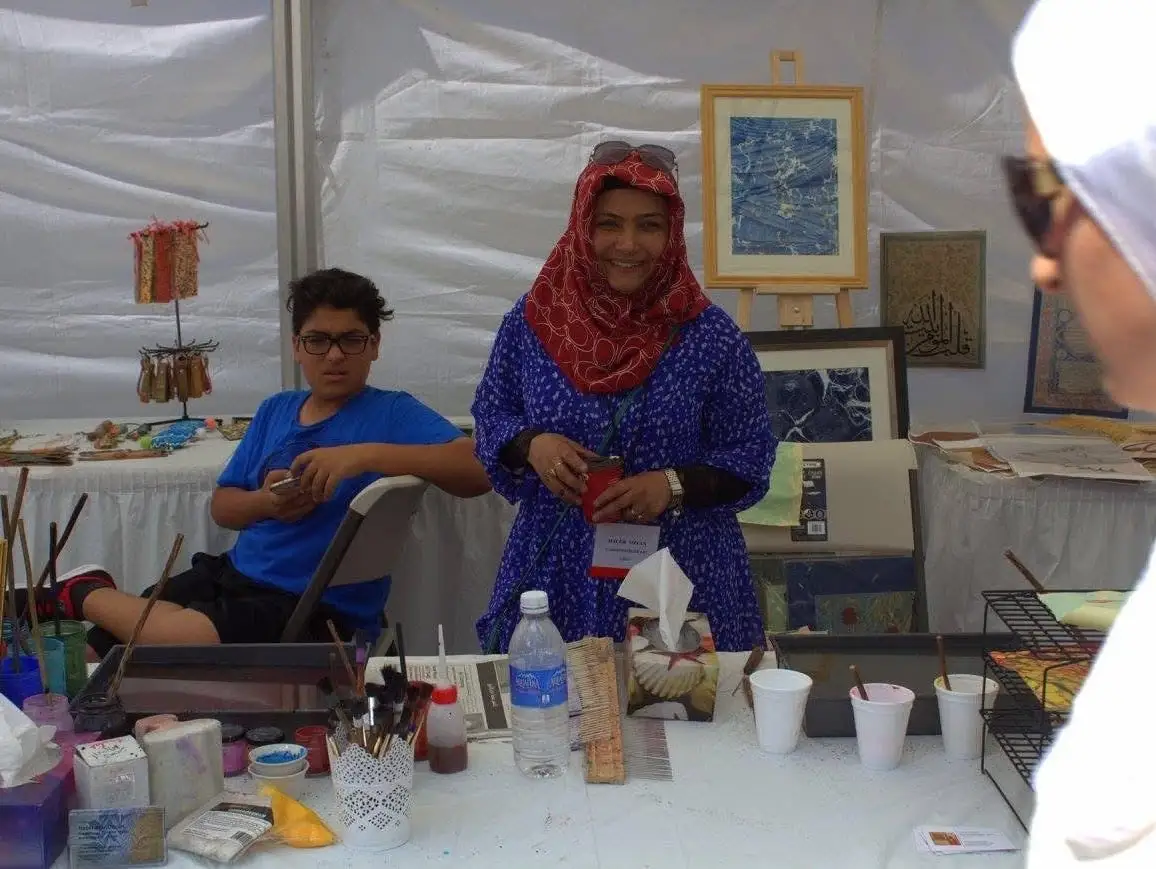 An artist at work at a painting stand, a boy watching beside her.
