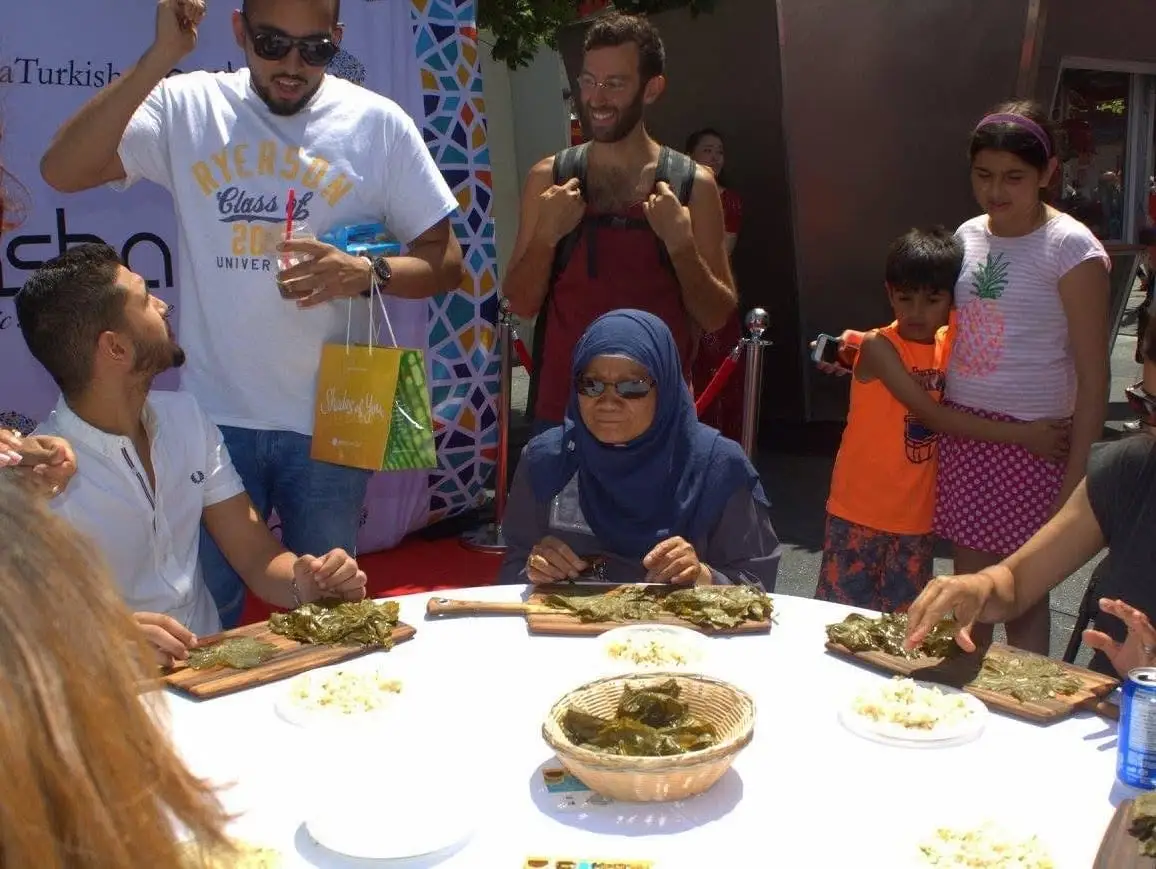 Visitors gather around a table of stuffed vine leaves on wooden boards.
