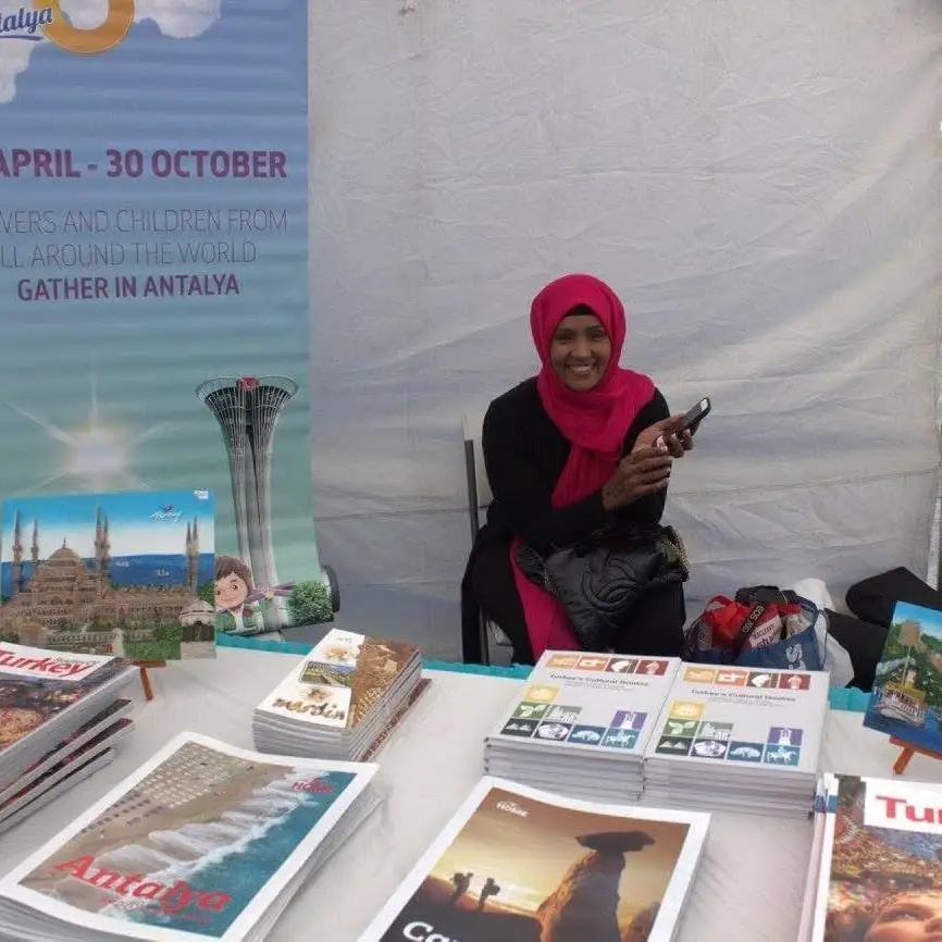 A woman sits at a stand stacked with travel brochures about Türkiye.