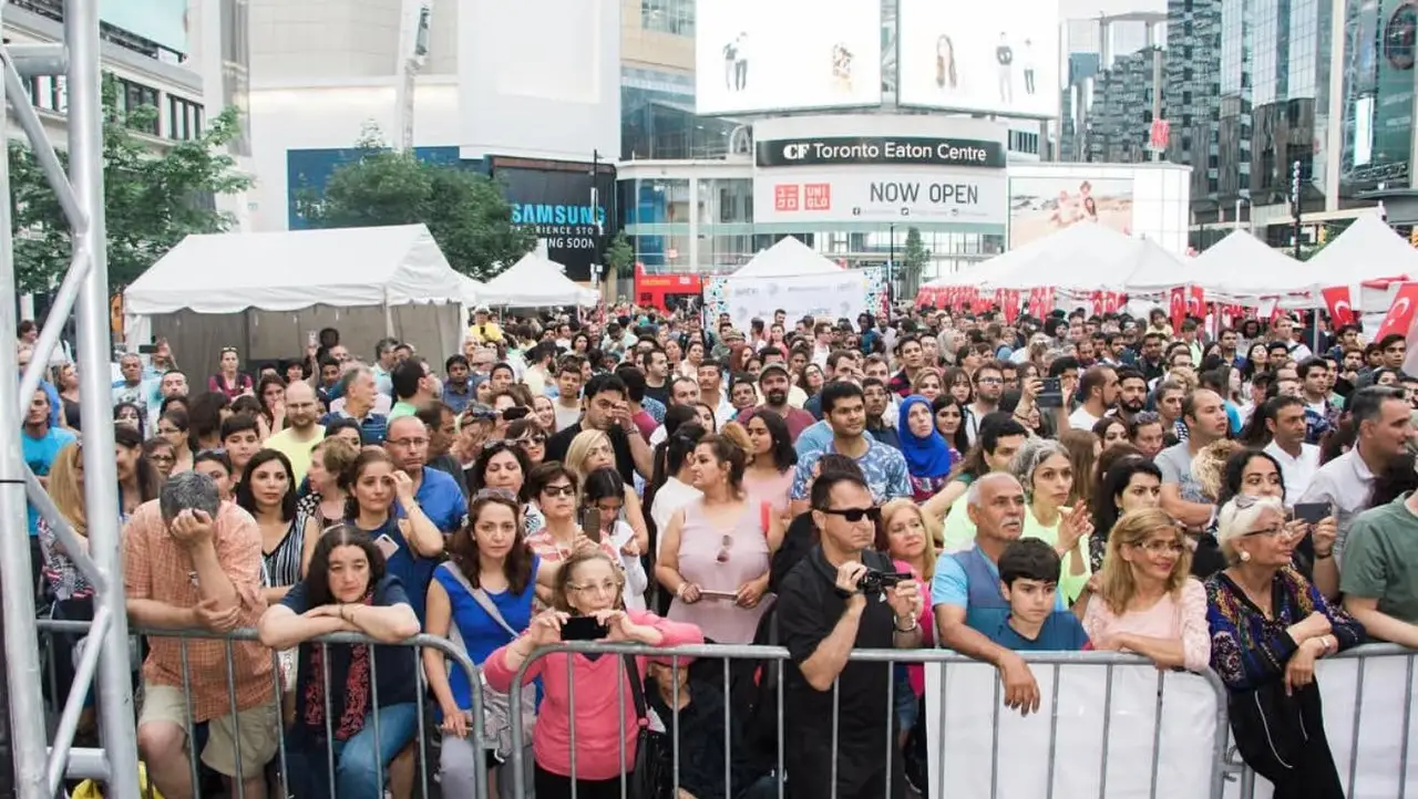 The crowd at the stage barrier on Yonge-Dundas Square, the Toronto Eaton Centre signs behind.