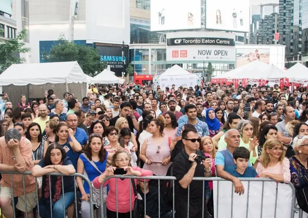 Festival-goers lean on the stage barrier, several filming on their phones, white tents behind.
