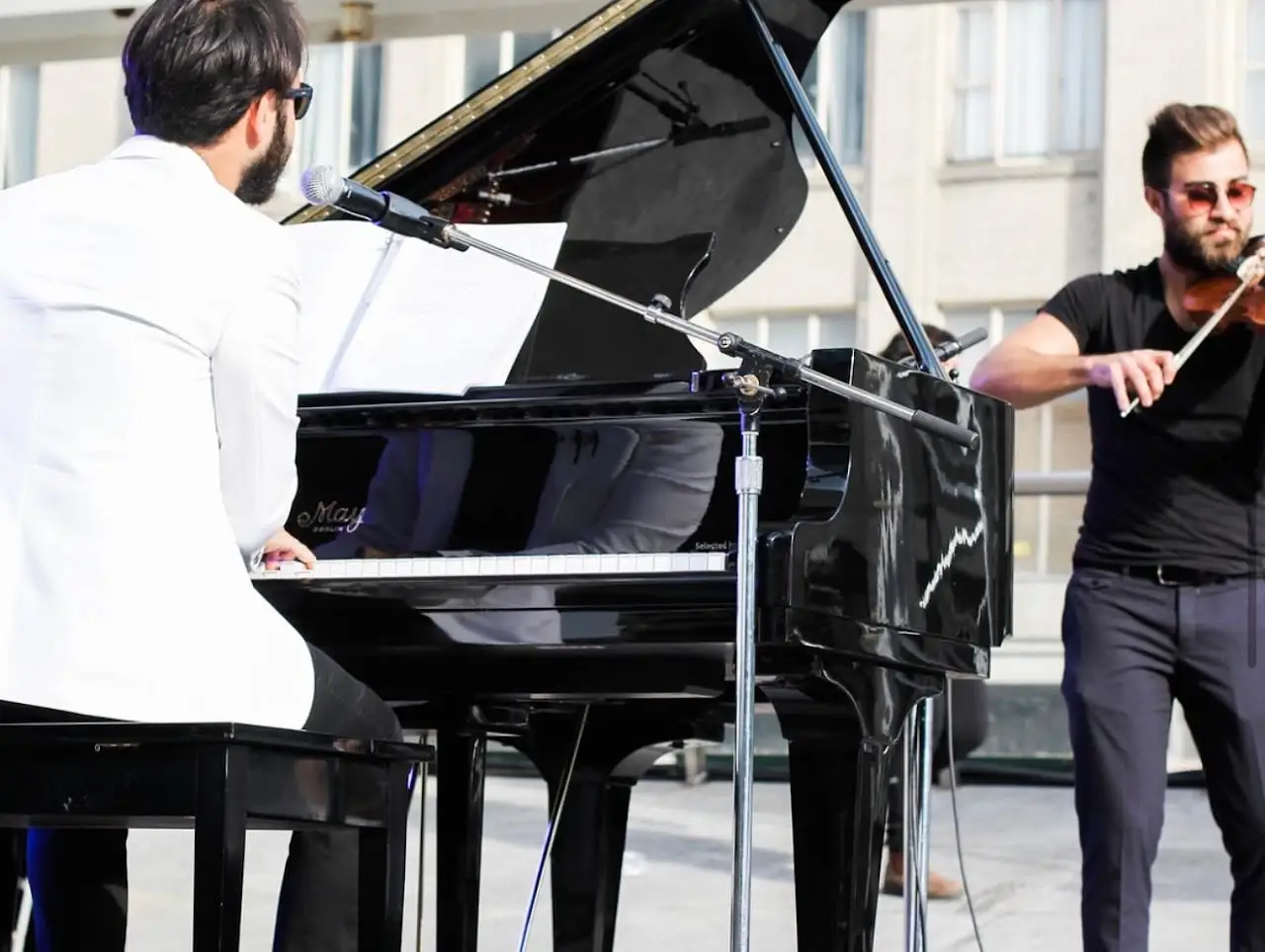 A pianist in a white jacket and a violinist perform on the outdoor stage.